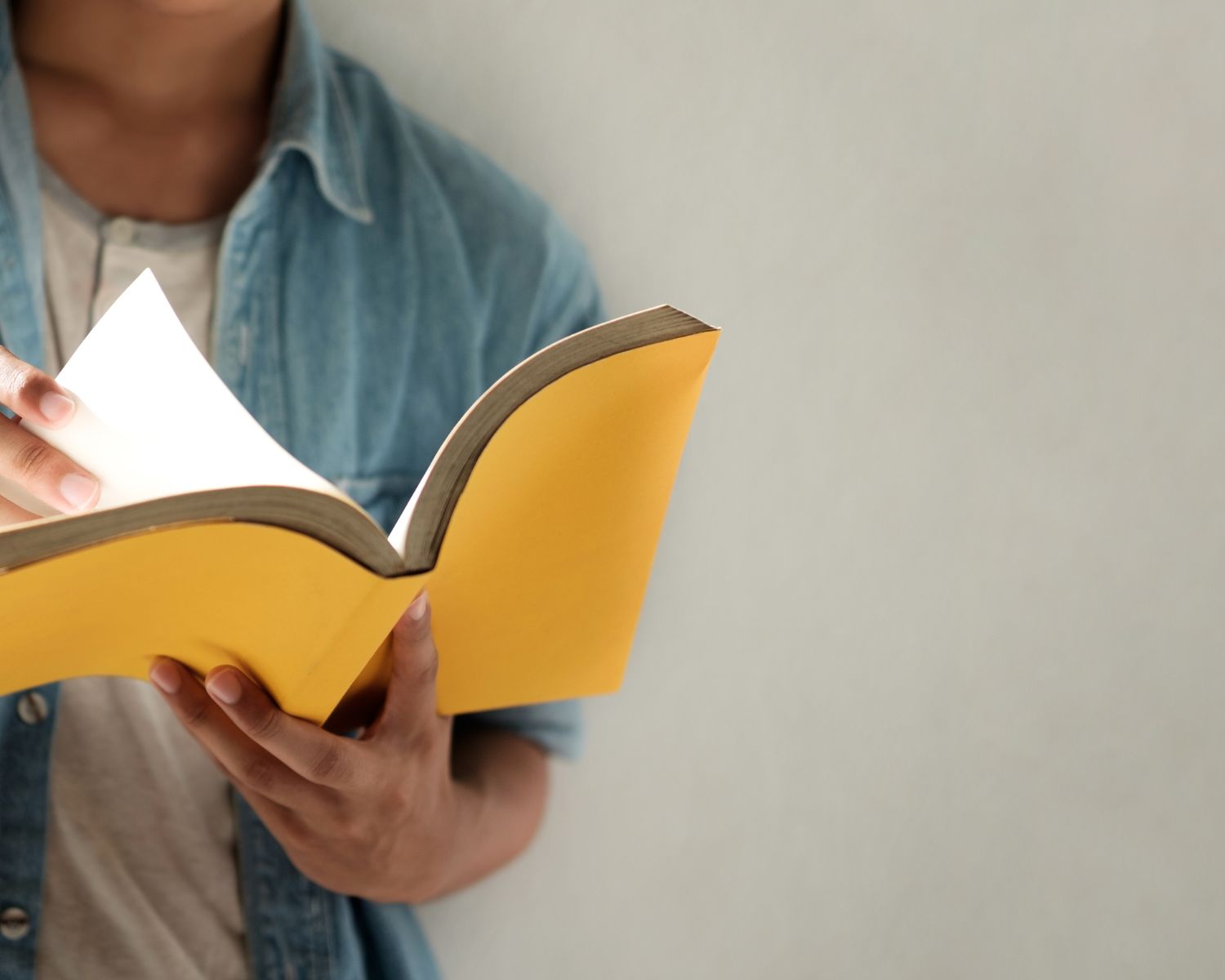 Person holding an open yellow book in front of a plain wall