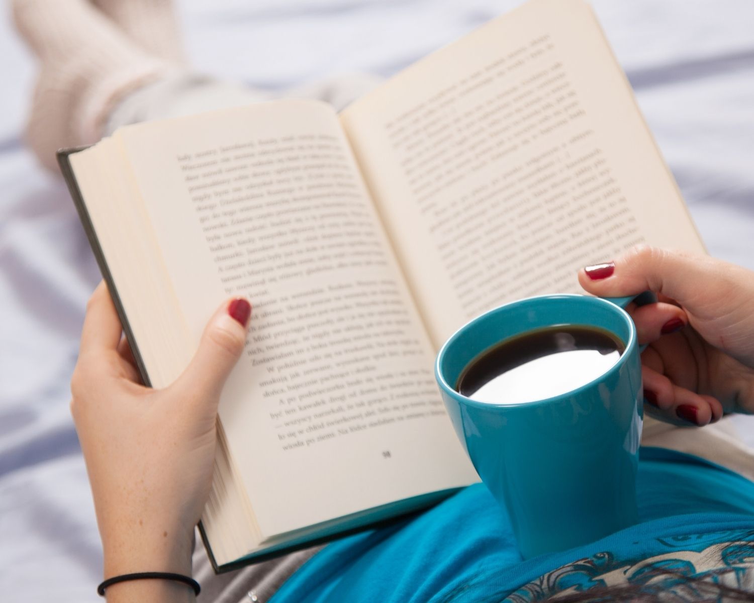A person holding a book on their lap and a coffee