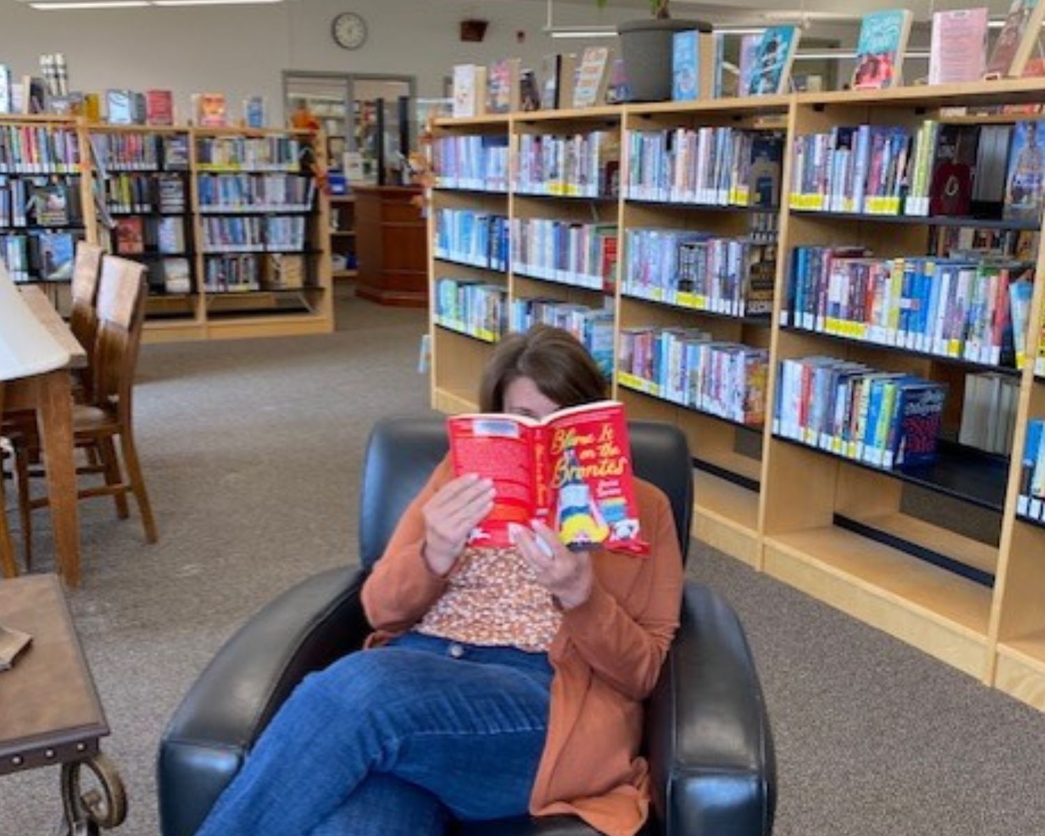 A picture of a PEPL staff member sitting in a black leather chair reading a book with a red cover