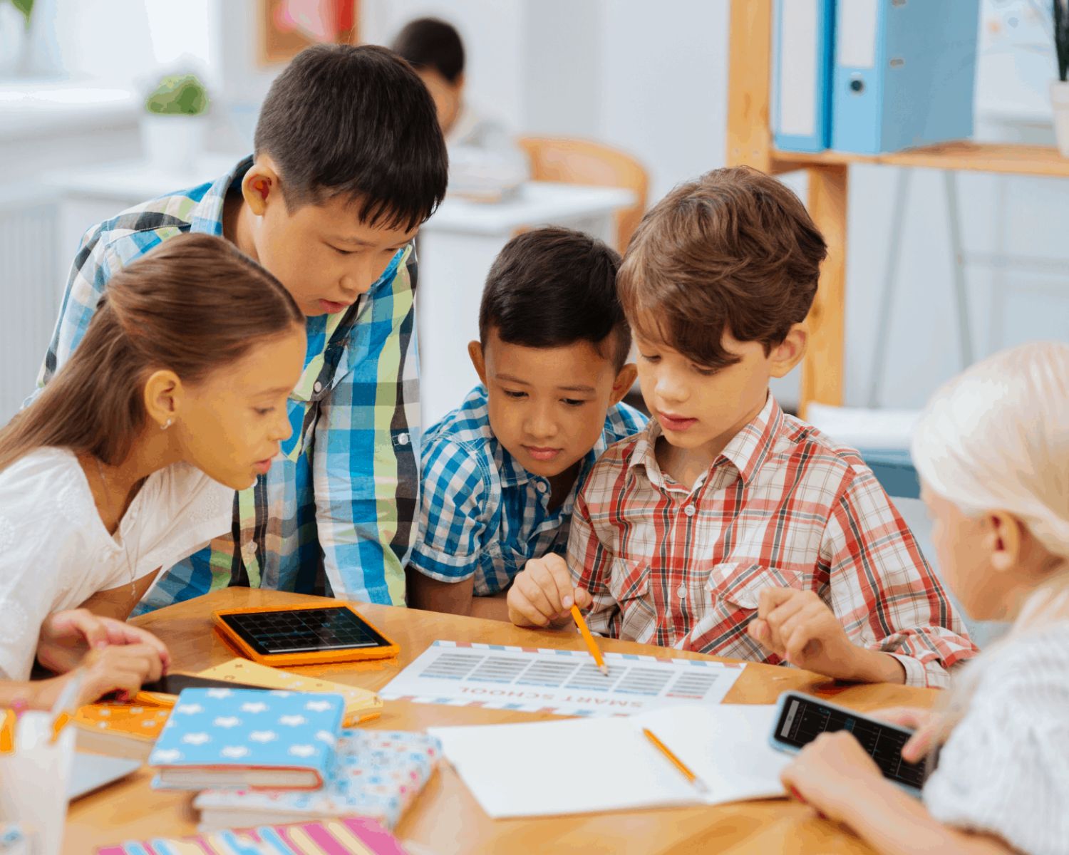 A group of children gathered holding pencils, looking at papers and devices